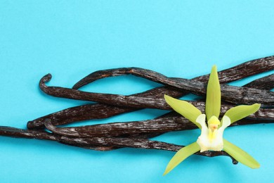 Photo of Vanilla pods and beautiful flower on light blue background, top view
