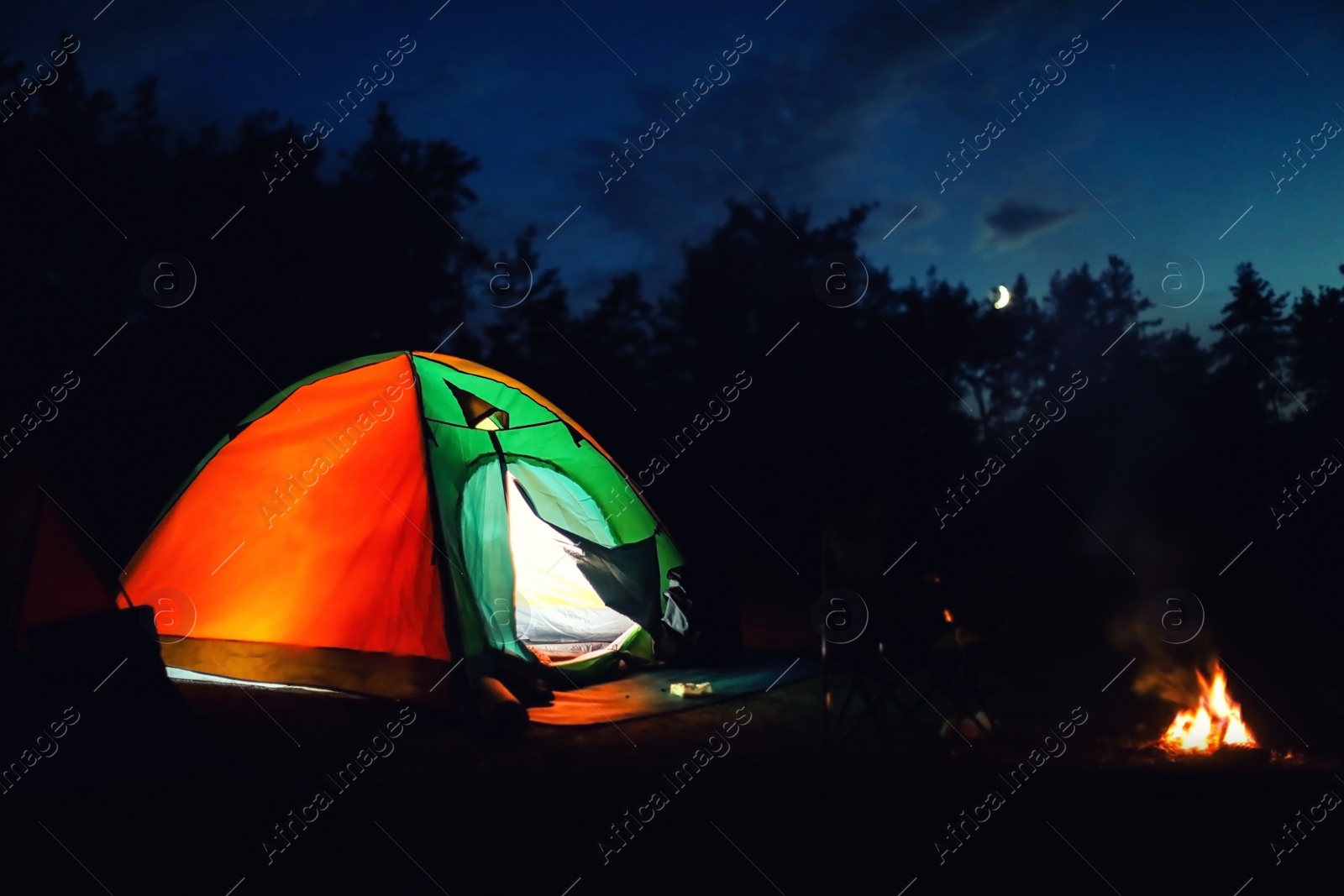 Photo of Glowing camping tent near bonfire in wilderness at night