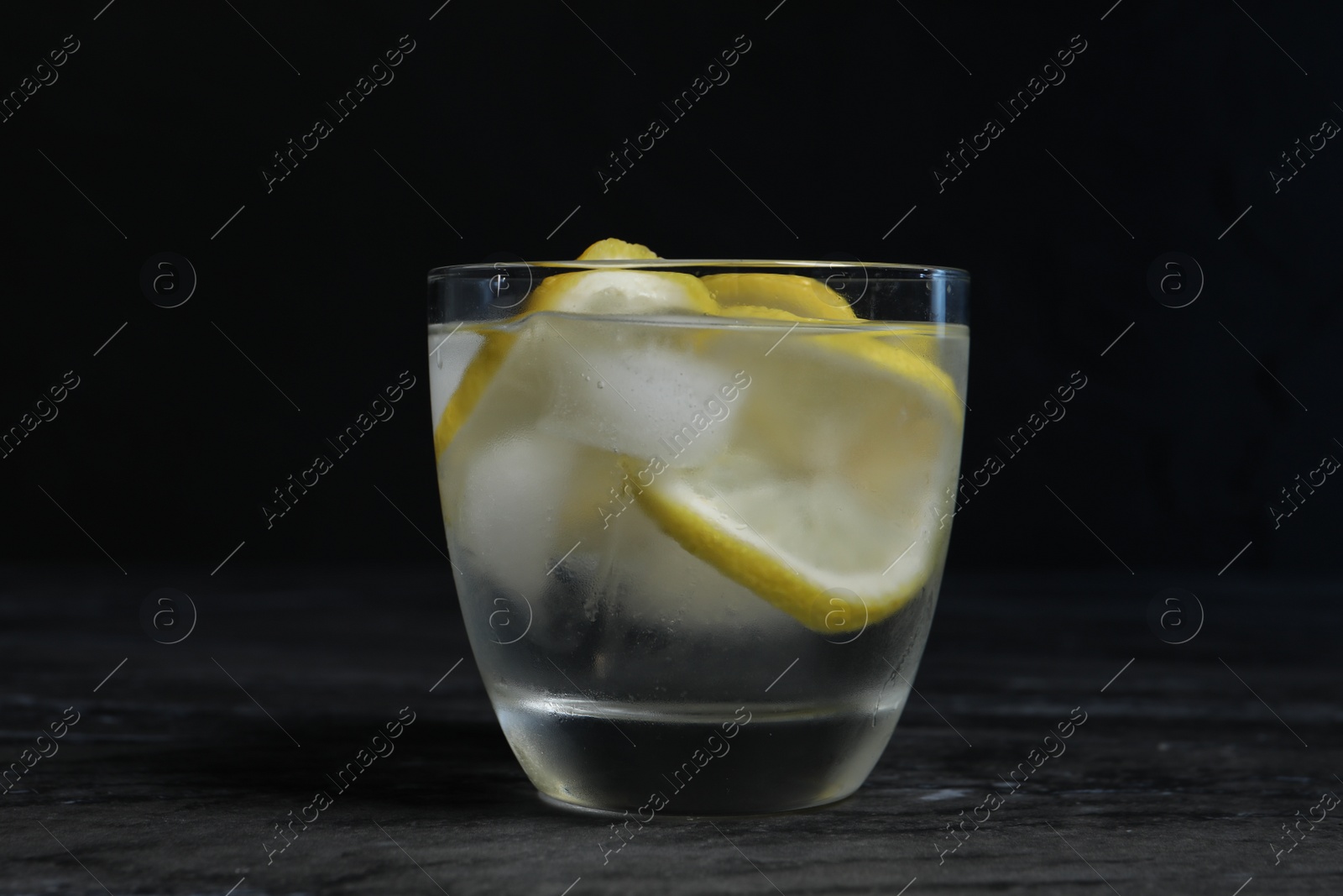 Photo of Glass of vodka with lemon slices and ice on grey table