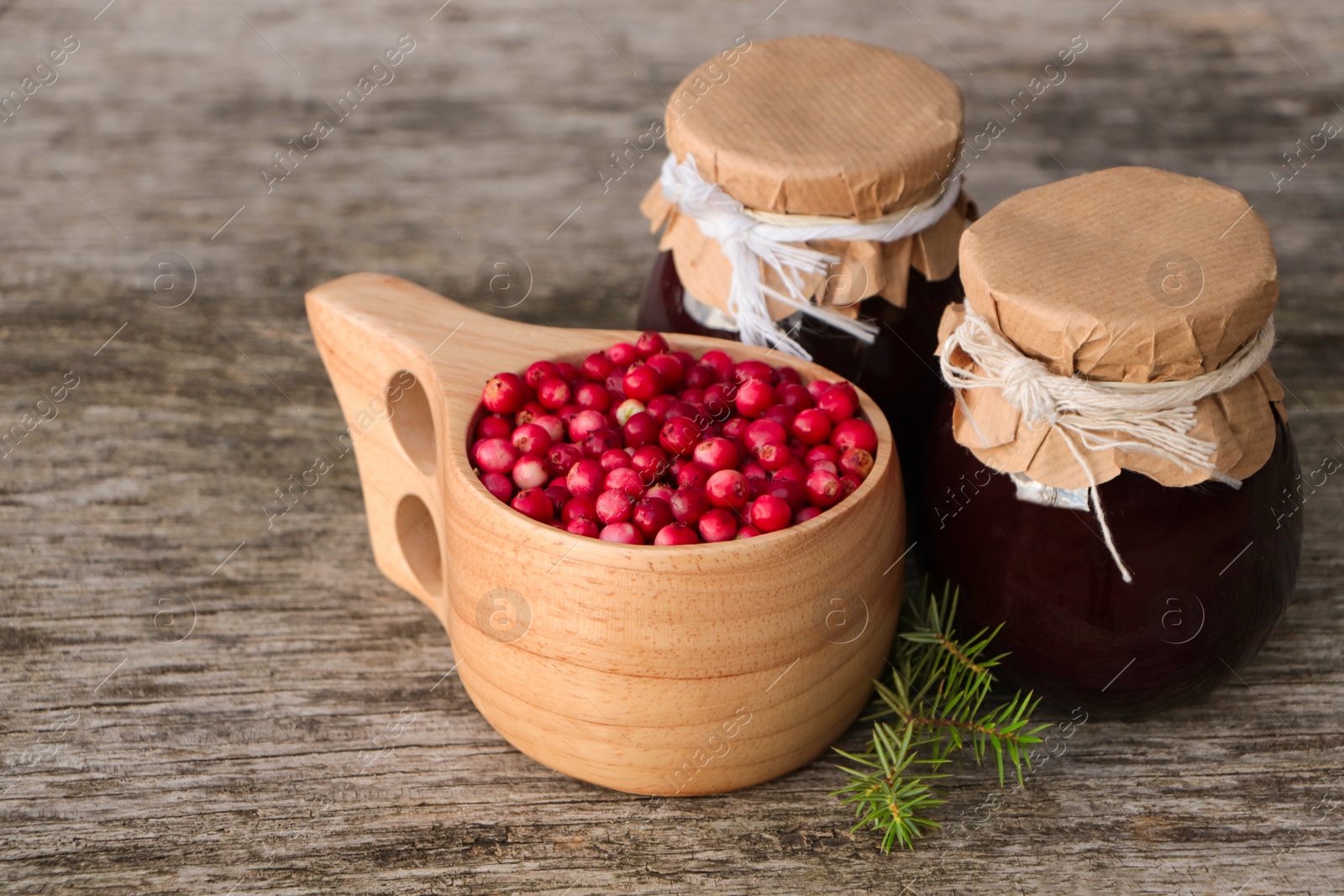 Photo of Tasty lingonberry jam in jars and cup with red berries on wooden table
