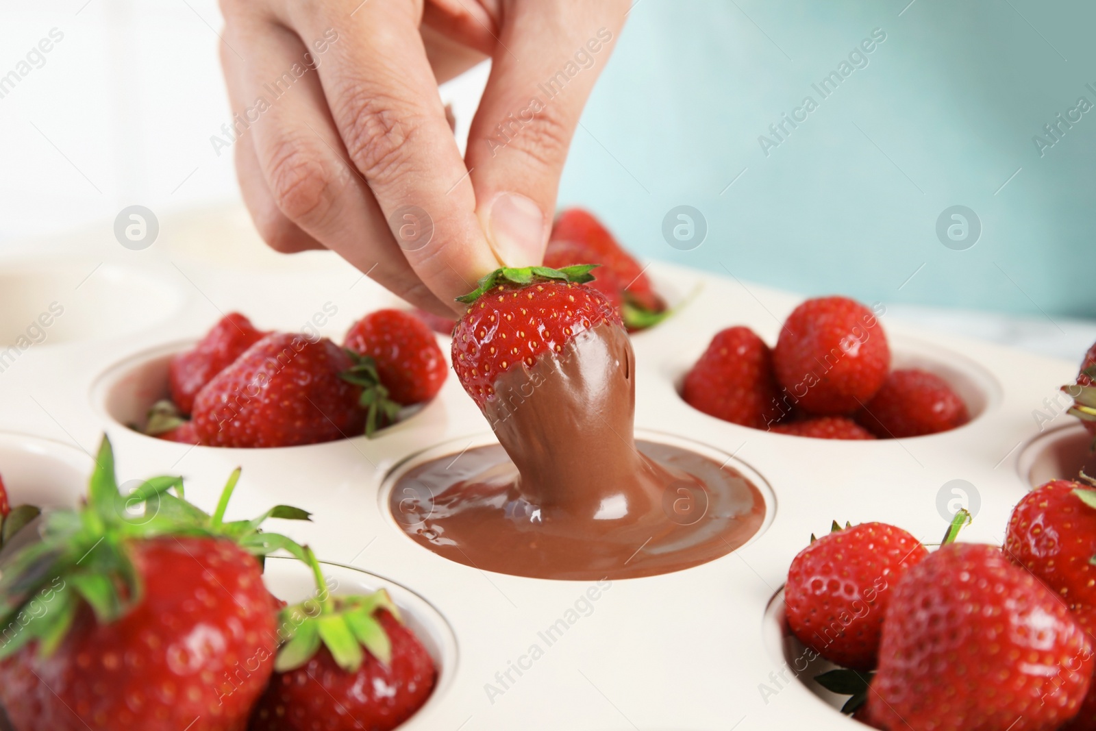 Photo of Woman dipping ripe strawberry into mold with melted chocolate, closeup