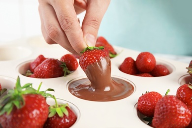 Woman dipping ripe strawberry into mold with melted chocolate, closeup