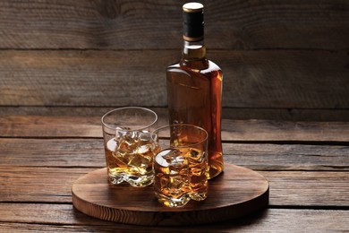 Photo of Whiskey with ice cubes in glasses and bottle on wooden table