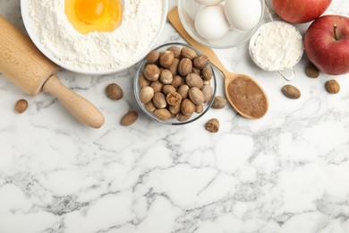 Photo of Nutmeg seeds and other ingredients on white marble table, flat lay. Space for text