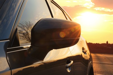 Photo of Black modern car parked on road at sunset, closeup of side view mirror