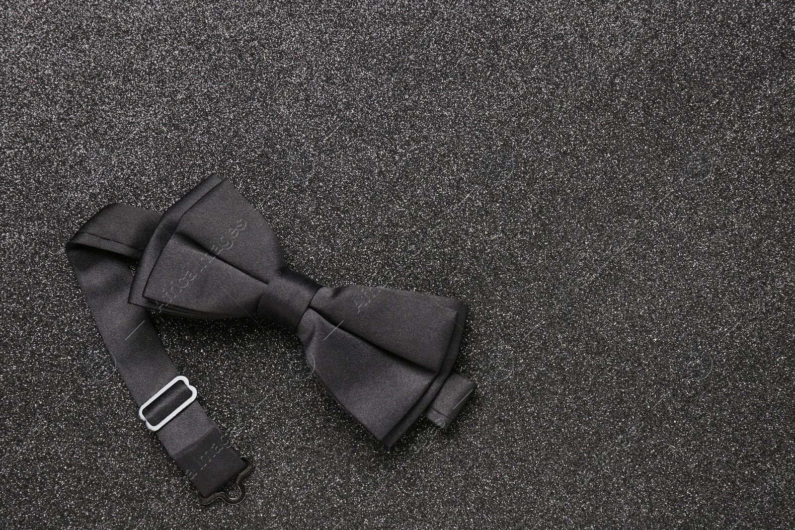 Photo of Stylish black bow tie on dark stone background, top view. Space for text