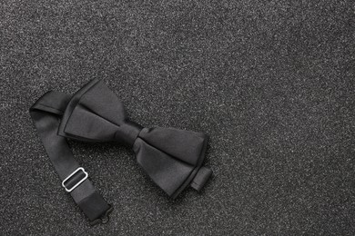 Photo of Stylish black bow tie on dark stone background, top view. Space for text