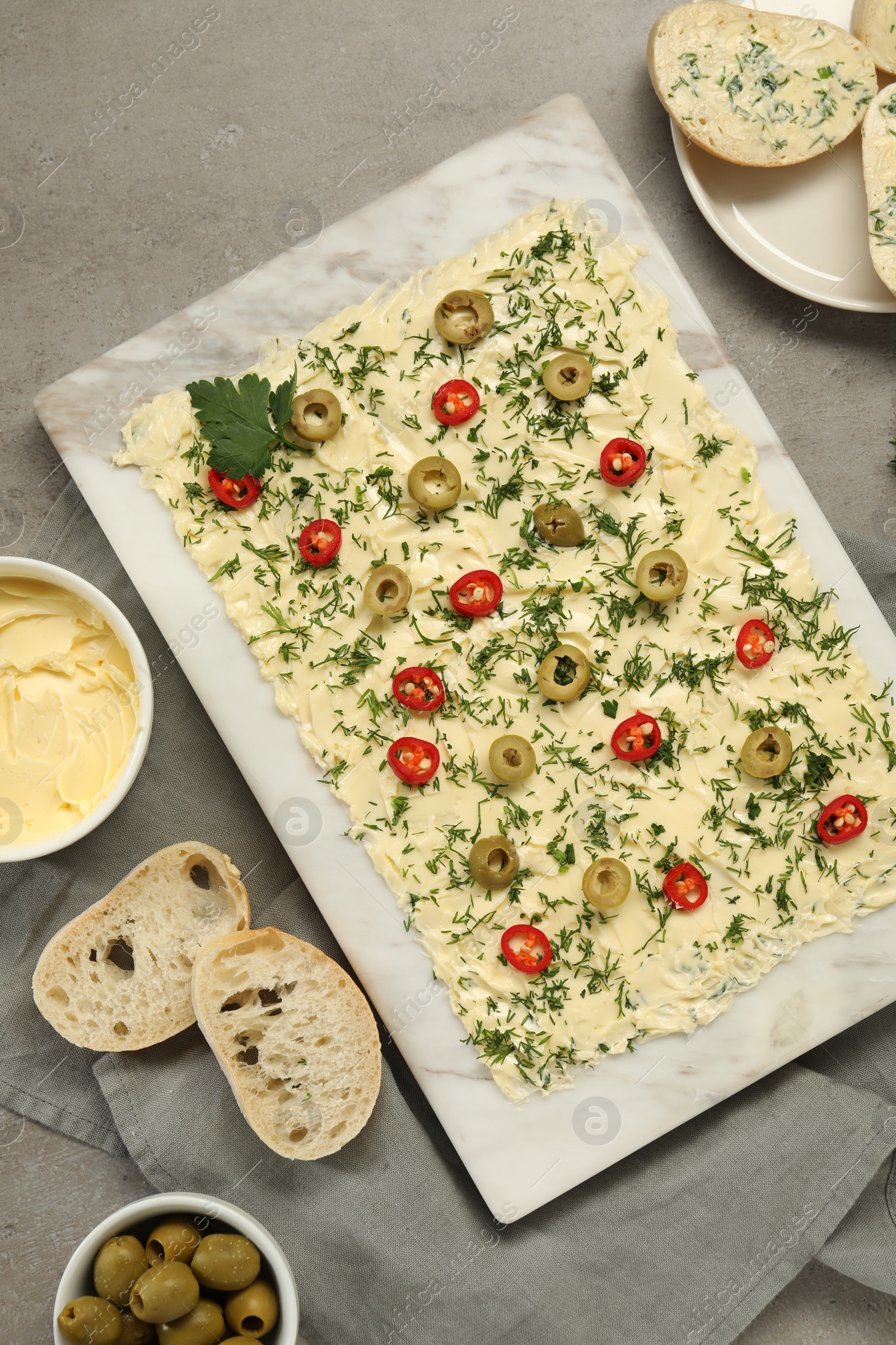 Photo of Fresh butter board with cut olives, pepper and bread on grey table, flat lay