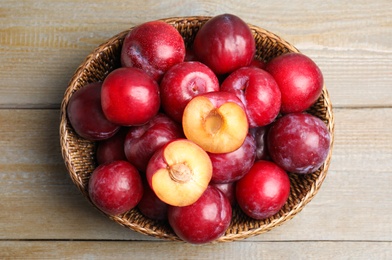 Photo of Delicious ripe plums in wicker bowl on wooden table, top view