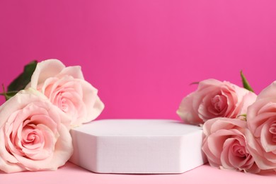 Photo of Stylish presentation for product. Podium and beautiful roses against pink background, space for text