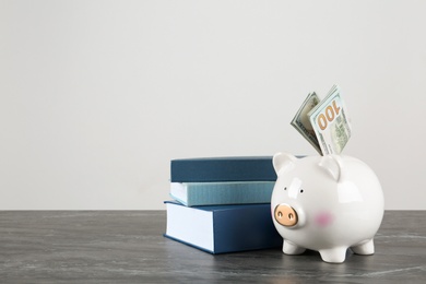 Piggy bank with dollars and books on table against white background. Space for text