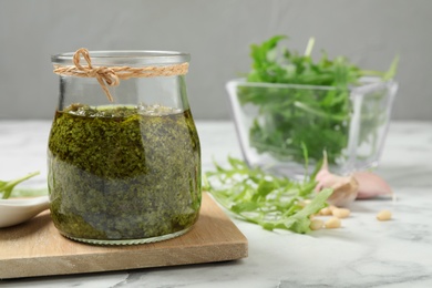 Jar of tasty arugula pesto and ingredients on white table