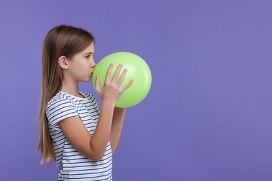 Photo of Girl inflating light green balloon on violet background, space for text