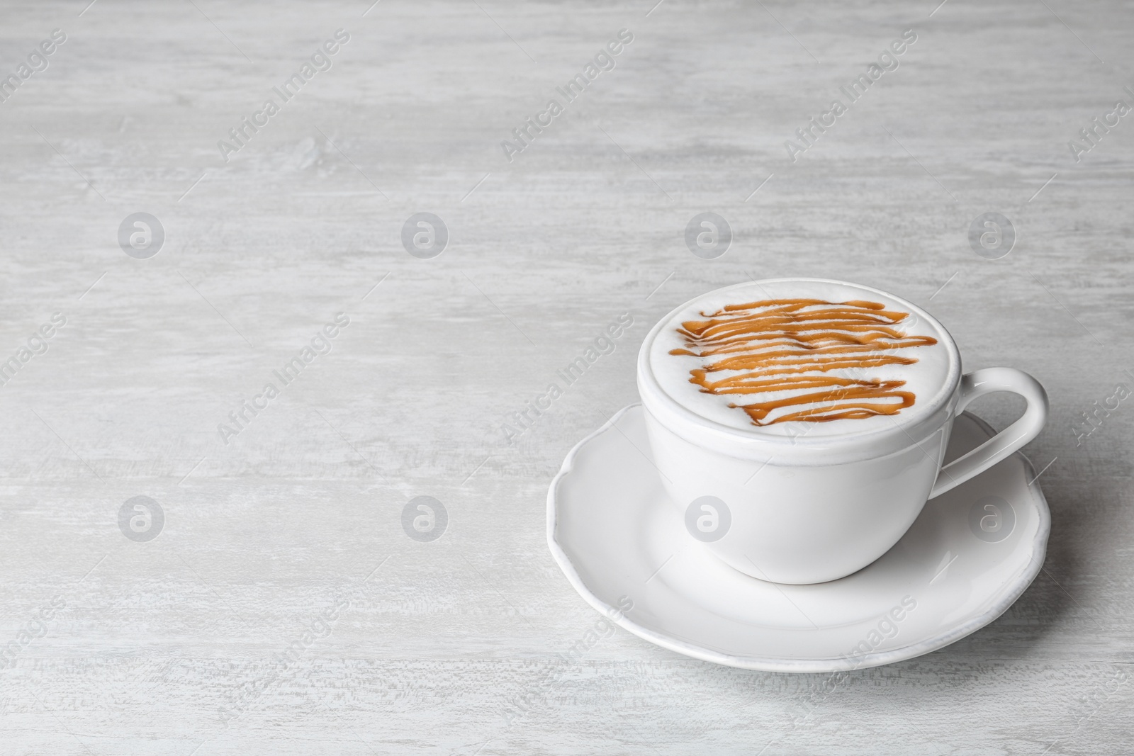 Photo of Cup of caramel macchiato on light table, space for text