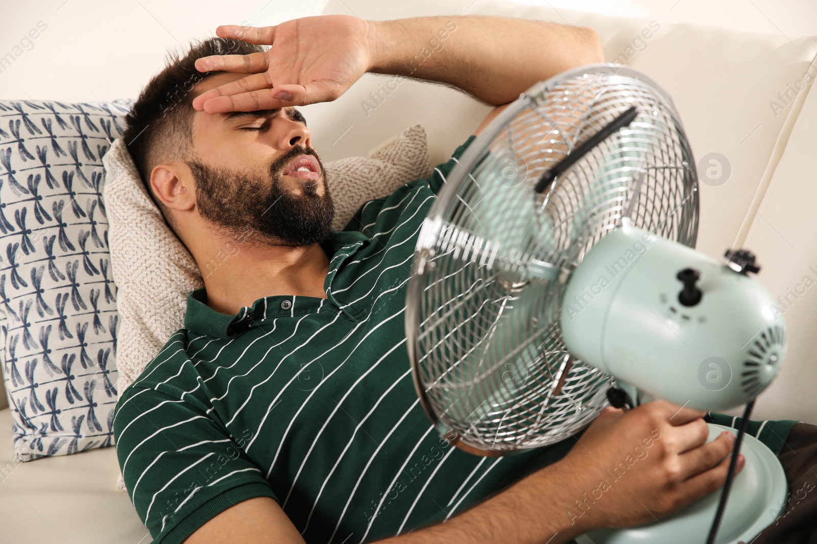 Photo of Man with fan suffering from heat at home. Summer season