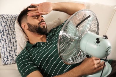 Man with fan suffering from heat at home. Summer season