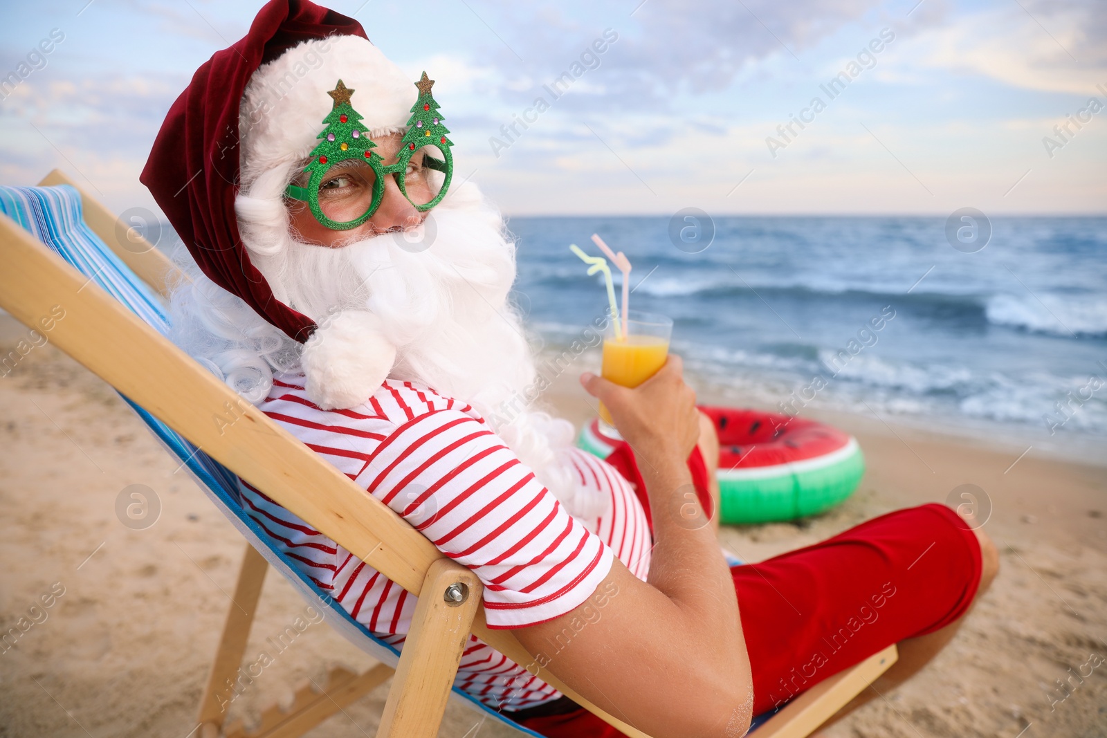 Photo of Santa Claus in party glasses with cocktail relaxing on beach. Christmas vacation