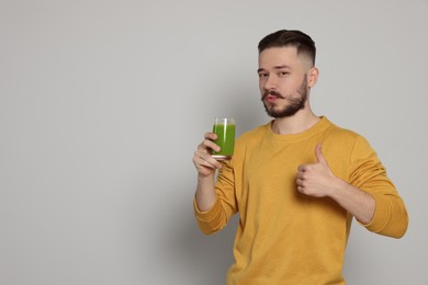 Photo of Handsome young man with glass of juice on light grey background. Space for text