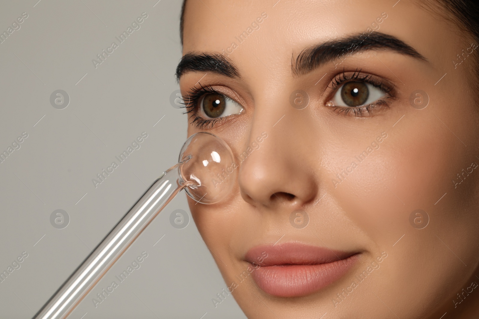 Photo of Woman using high frequency darsonval device on grey background, closeup