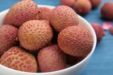 Photo of Fresh ripe lychee fruits in bowl on blue table, closeup