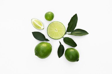 Photo of Whole and cut fresh limes with leaves on white background, flat lay