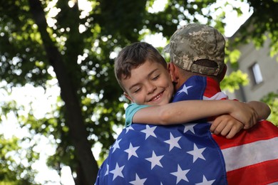 Photo of Soldier with flag of USA and his little son hugging outdoors