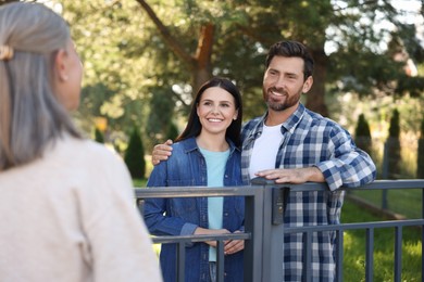 Photo of Friendly relationship with neighbours. Happy young couple and senior woman near fence outdoors