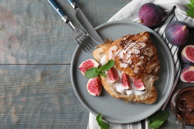 Photo of Delicious croissant with figs and cream served on light blue wooden table, flat lay. Space for text