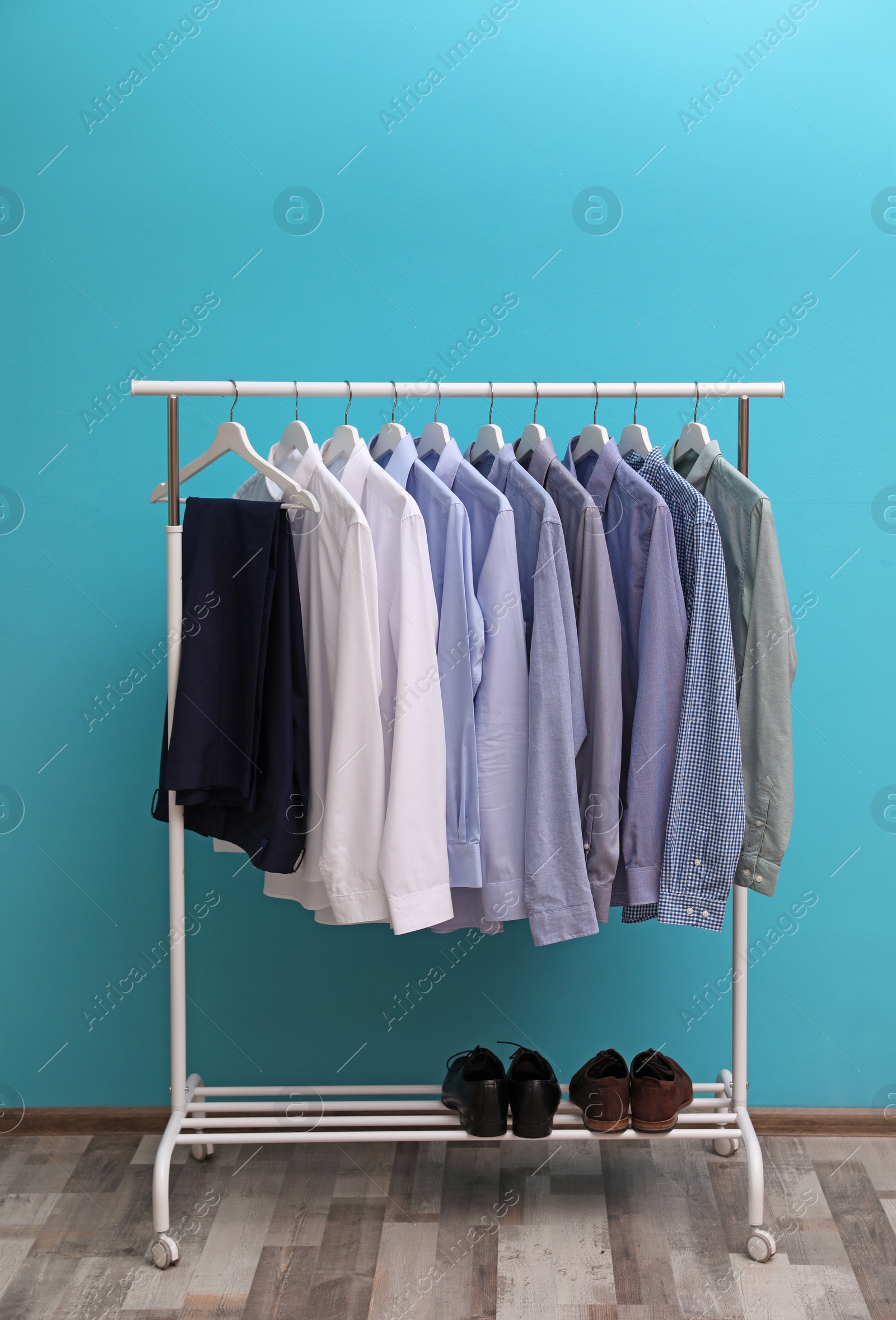 Photo of Wardrobe rack with men's clothes and shoes near color wall