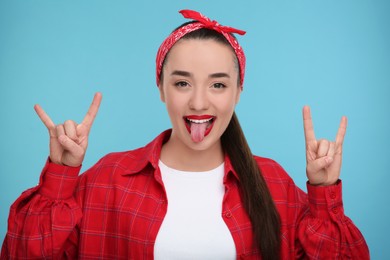 Photo of Happy woman showing her tongue and rock gesture on light blue background