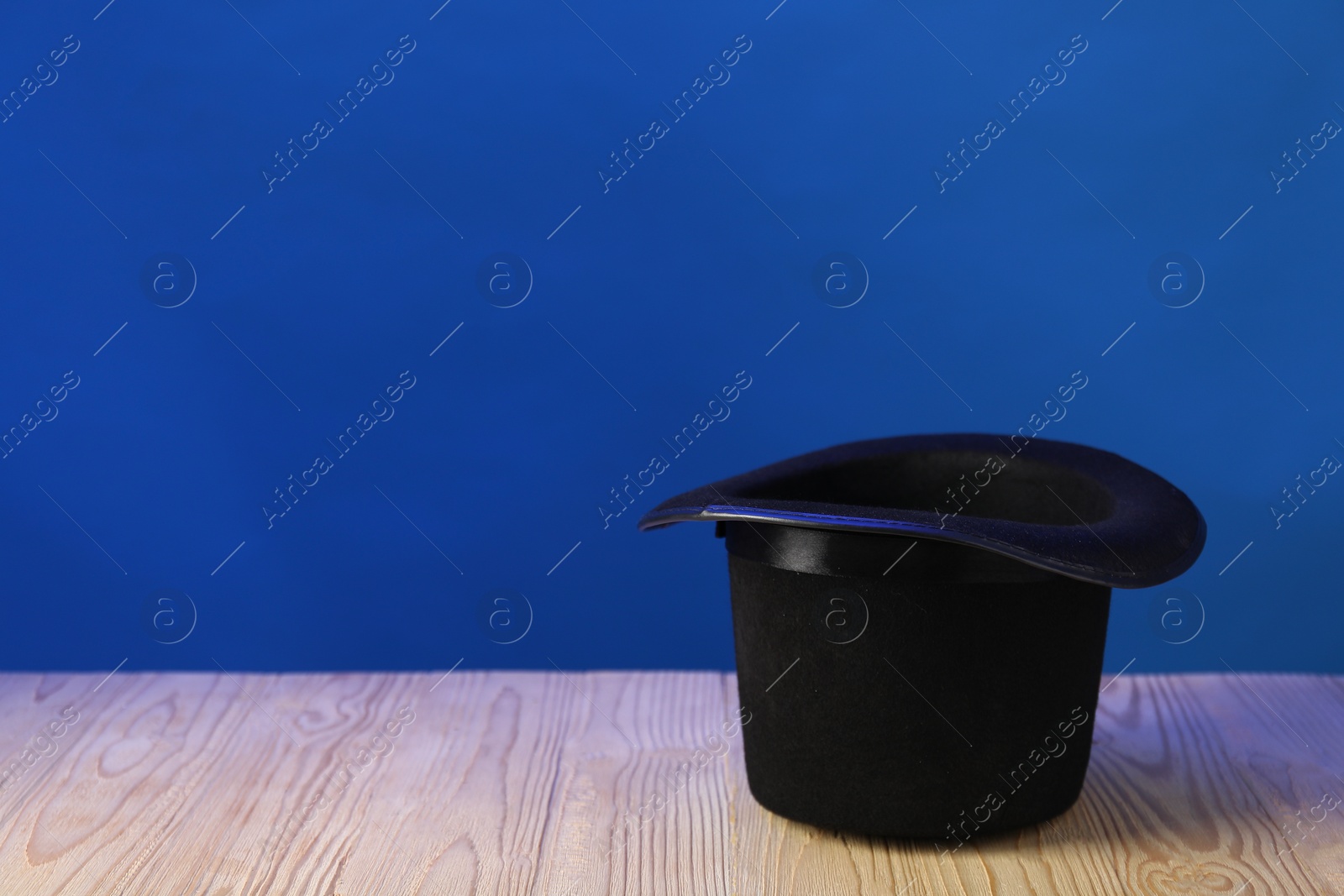 Photo of Magician's hat on wooden table against blue background, space for text