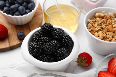 Photo of Fresh berries, tasty oatmeal and honey on white table, closeup. Healthy breakfast