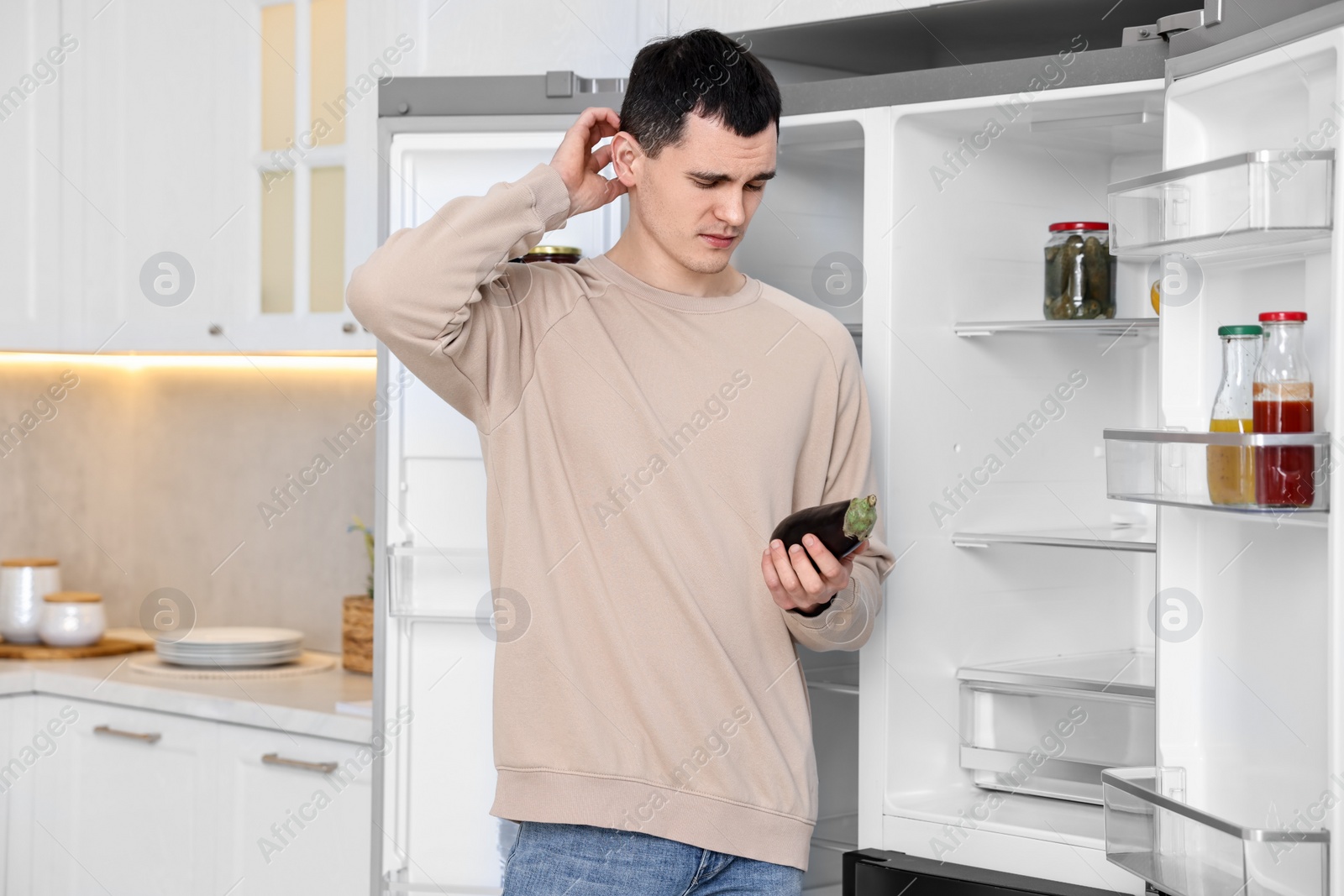 Photo of Upset man with eggplant near empty refrigerator in kitchen