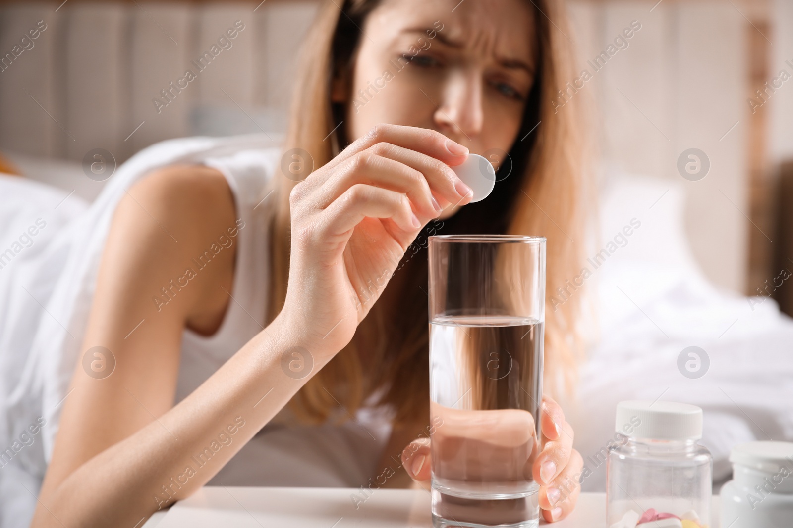 Photo of Woman putting medicine for hangover into glass of water at home, focus on hand with pill