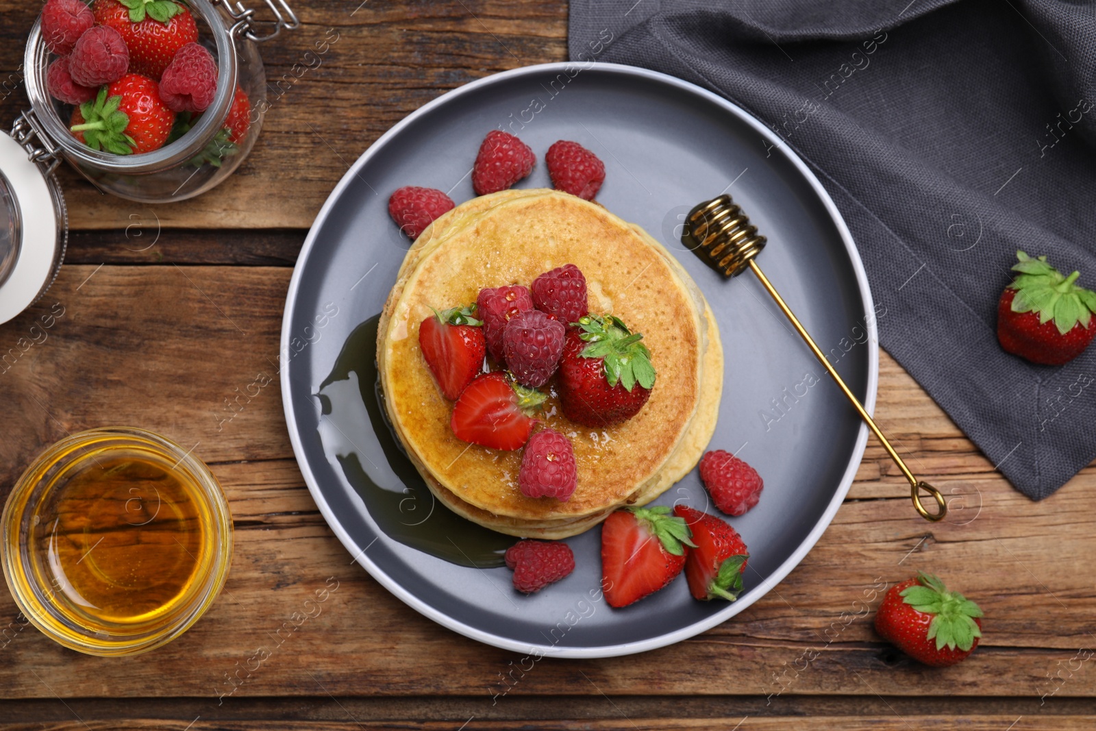 Photo of Tasty pancakes served with fresh berries and honey on wooden table, flat lay