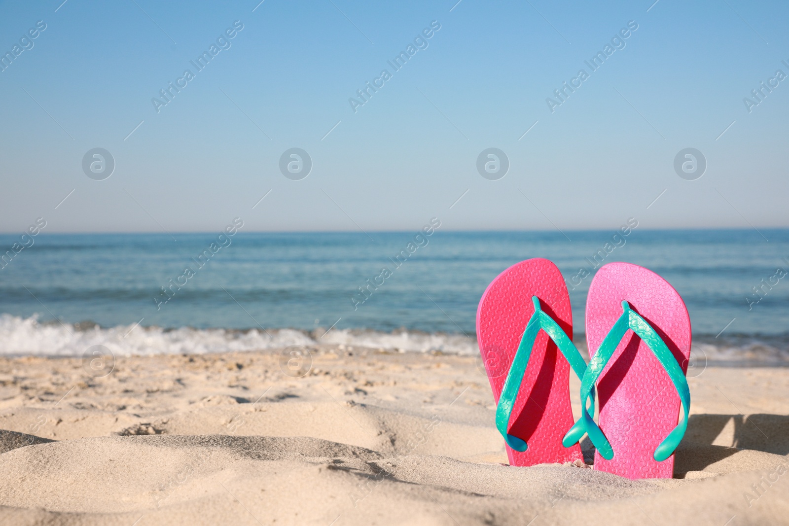 Photo of Stylish flip flops in sand on beach. Space for text