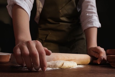 Photo of Woman rolling fresh dough at wooden table, closeup. Cooking grissini