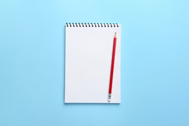 Photo of Notebook and pencil on light blue background, top view
