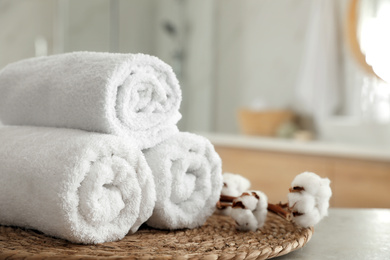 Photo of Clean rolled towels and cotton flowers on table in bathroom