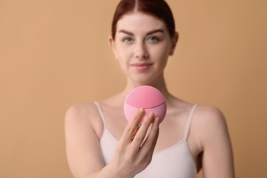 Washing face. Young woman with cleansing brush on beige background, selective focus