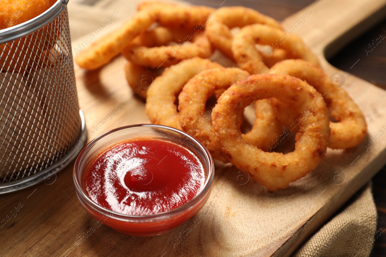 Photo of Tasty ketchup and onion rings on wooden board, closeup