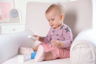 Cute baby girl playing with building blocks in armchair at home
