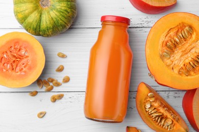 Photo of Tasty pumpkin juice in glass bottle and different pumpkins on white wooden table, flat lay