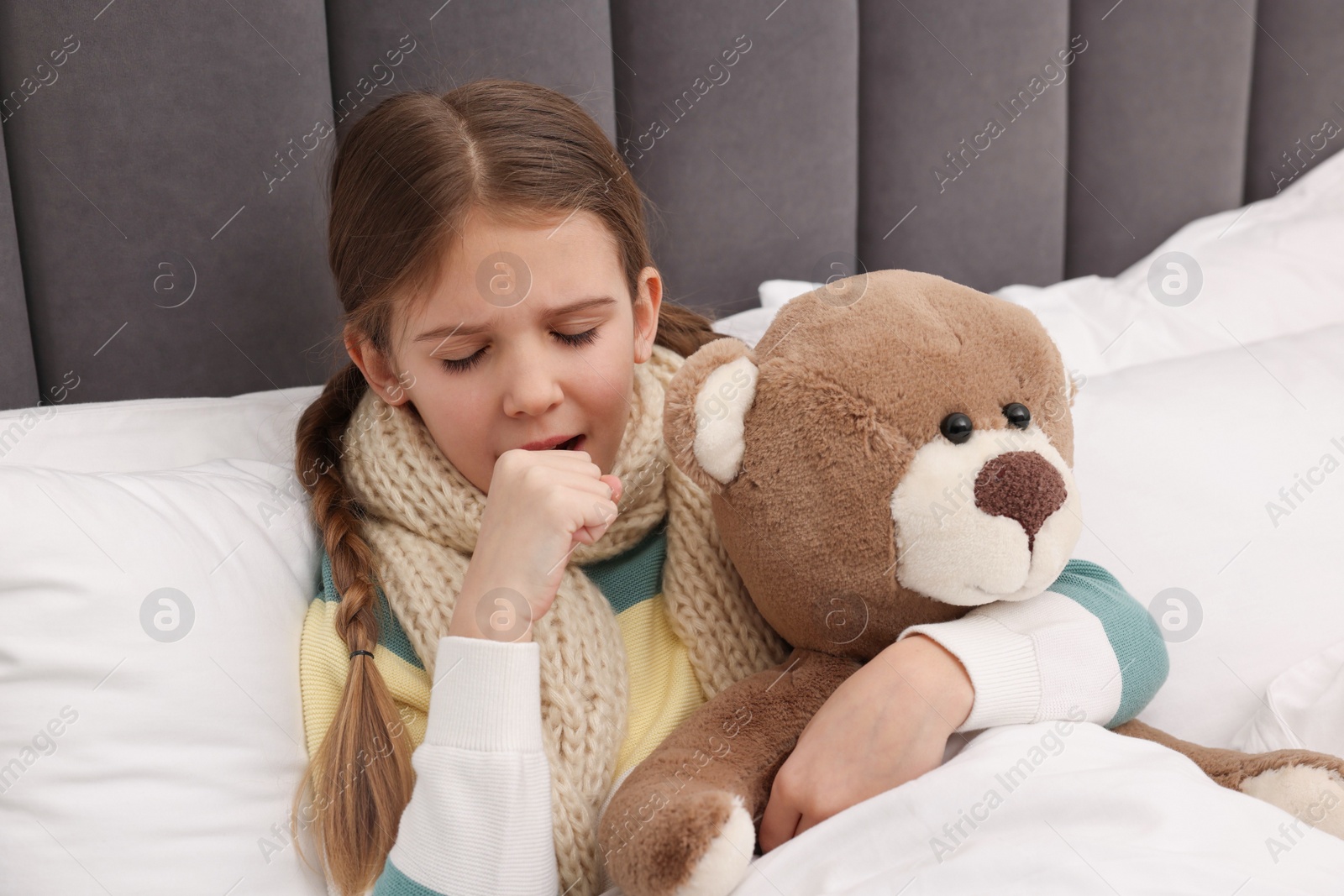 Photo of Sick girl with teddy bear coughing on bed at home