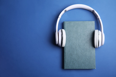 Book and modern headphones on blue background, top view. Space for text