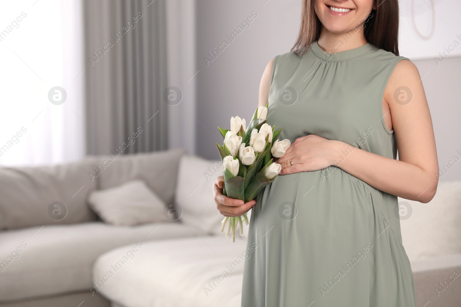 Photo of Young pregnant woman with flowers at home, closeup. Space for text