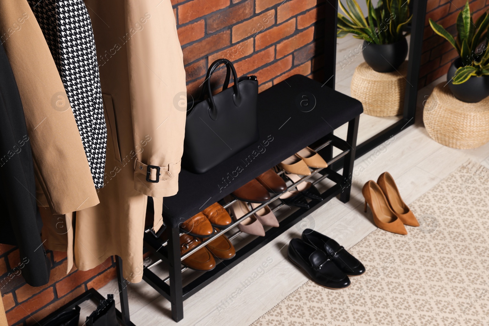 Photo of Stylish hallway with shoe storage bench and accessories near brick wall. Interior design