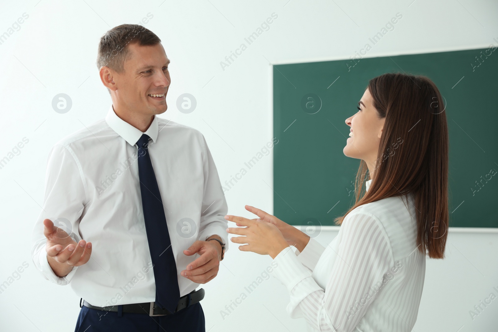 Photo of Man and woman talking near green chalkboard in classroom