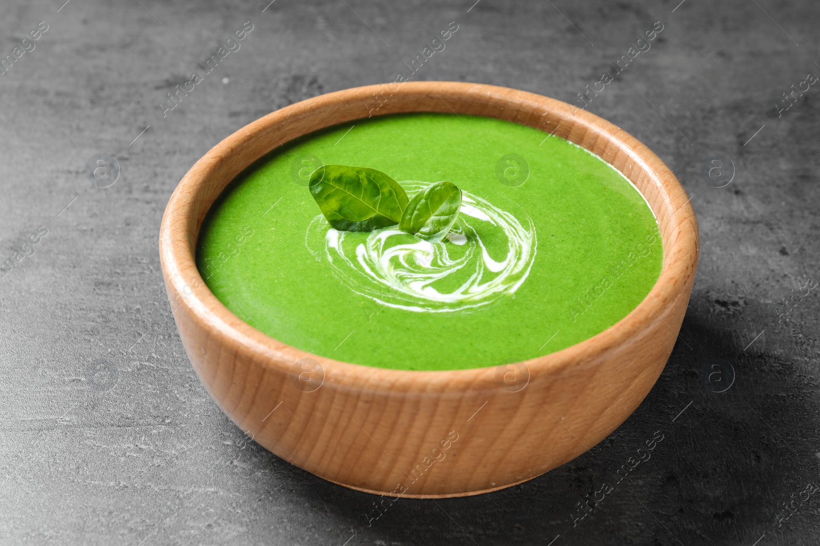 Photo of Bowl of healthy green soup with fresh spinach on grey table