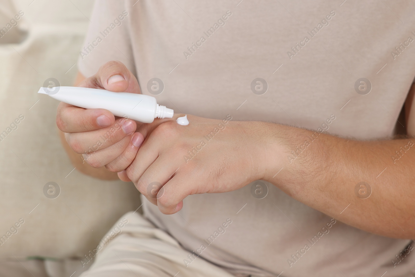 Photo of Man applying hand cream from tube at home, closeup